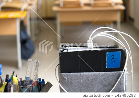 Digital Tablets Charging in Classroom with Stationery Supplies on Desk During School Day Digital Tablets Charging in Classroom with Stationery Supplies on Desk During School Day 142496298