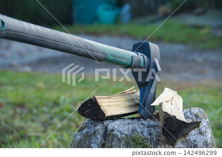 Axe splitting wood on a tree stump, a close view of the tool in action outdoors. Axe splitting wood on a tree stump, a close view of the tool in action outdoors. 142496299