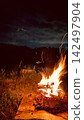 A campfire lit at a campsite at night, with large flames rising (sparks and firewood). 142497904