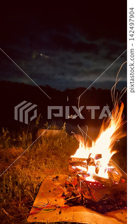 夜晚,露營地燃起營火,熊熊烈焰升騰(火花和柴火)。 夜晚,露營地燃起營火,熊熊烈焰升騰(火花和柴火)。 142497904