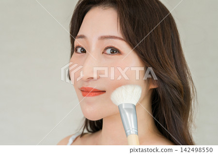 一張女性用化妝刷給臉頰上妝的美麗照片。 一張女性用化妝刷給臉頰上妝的美麗照片。 142498550