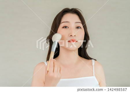 A beauty image of a woman applying makeup to her cheeks with a makeup brush. A beauty image of a woman applying makeup to her cheeks with a makeup brush. 142498587