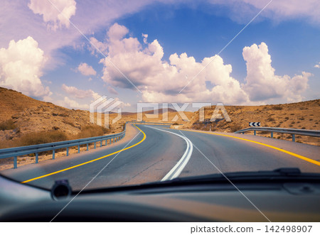 Driving a car on the mountain road in the desert. View of sandstone mountains through the windscreen. The road from Arad to the Dead Sea. Israel Driving a car on the mountain road in the desert. View of sandstone mountains through the windscreen. The road from Arad to the Dead Sea. Israel 142498907