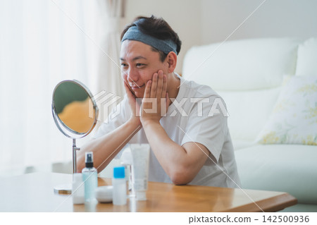 一位四十多歲的男子對著鏡子檢查自己的下顎線條，臉上露出笑容，他雙手攏在臉頰上，這是他男士護膚程序的一部分。 142500936