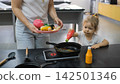 Little girl playing together with mother at a play kitchen preparing a dish with toy seafood and vegetables. Family cooking play concept 142501346