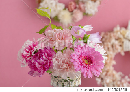 A bouquet in a vase and a flower wreath (gerberas and carnations) stand out against a pink background. A bouquet in a vase and a flower wreath (gerberas and carnations) stand out against a pink background. 142501856