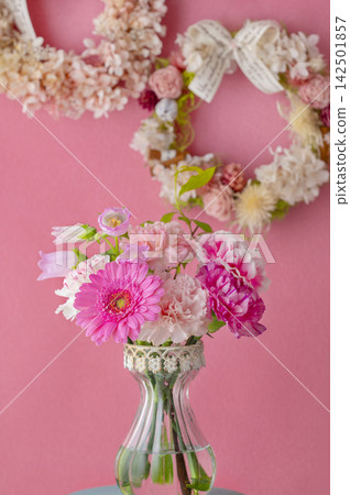A bouquet in a vase and a flower wreath (gerberas and carnations) stand out against a pink background. A bouquet in a vase and a flower wreath (gerberas and carnations) stand out against a pink background. 142501857