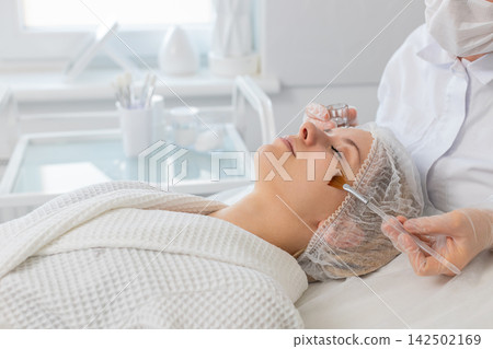 Beautician applying special moisturizing acid serum peeling face cheek of young woman in clinic Beautician applying special moisturizing acid serum peeling face cheek of young woman in clinic 142502169