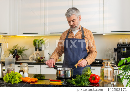 Middle-aged man cooking healthy soup on electric stove in home kitchen for diet nutrition lifestyle 142502171