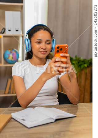 African American young woman on home table learning foreign language and repeating words on phone African American young woman on home table learning foreign language and repeating words on phone 142502272