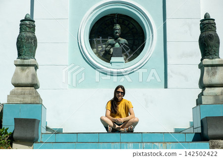 Young woman sitting cross-legged on sunny steps in front of historic architecture Young woman sitting cross-legged on sunny steps in front of historic architecture 142502422