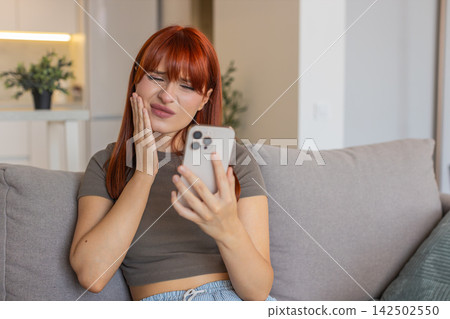 Young woman with smartphone holds cheek sore tooth opens dentist contacts and schedules online visit Young woman with smartphone holds cheek sore tooth opens dentist contacts and schedules online visit 142502550