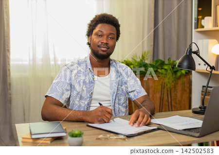 African American young man on home table reads contract then signs document with a satisfied smile African American young man on home table reads contract then signs document with a satisfied smile 142502583