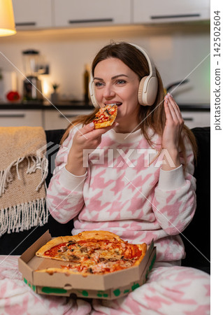 Adult woman dances with headphones at night enjoys music eats pizza smiles freedom happy cozy moment Adult woman dances with headphones at night enjoys music eats pizza smiles freedom happy cozy moment 142502604