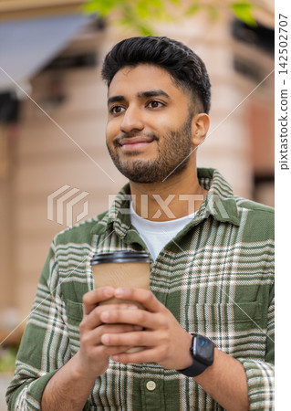 Indian man drinking coffee walking in city street smiling during peaceful morning stroll outdoors Indian man drinking coffee walking in city street smiling during peaceful morning stroll outdoors 142502707