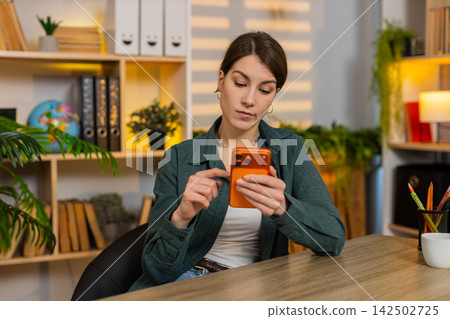 Young woman on home table scrolling smartphone feeling bored tired during remote work break indoors Young woman on home table scrolling smartphone feeling bored tired during remote work break indoors 142502725