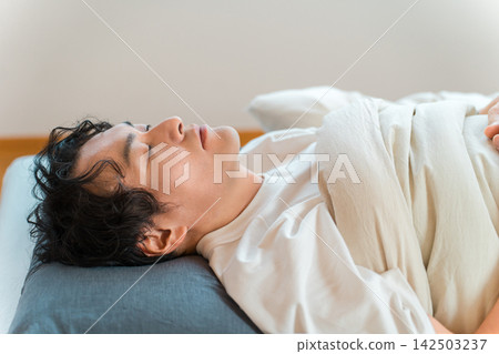 A man sleeping on his back in bed; an image related to sleep and health management. A man sleeping on his back in bed; an image related to sleep and health management. 142503237