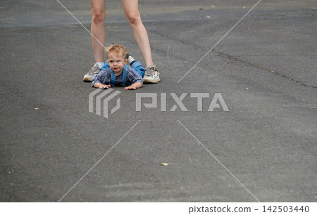 Naughty little boy lying on asphalt road and refusing to walk during stroll with mother. Naughty little boy lying on asphalt road and refusing to walk during stroll with mother. 142503440
