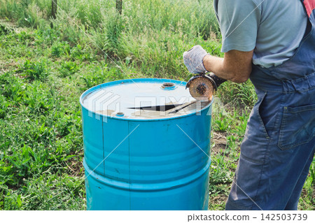 Worker cutting an old steel drum with an angle grinder. Upcycling metal barrel Worker cutting an old steel drum with an angle grinder. Upcycling metal barrel 142503739