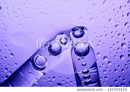 Two pipettes transferring cosmetic liquid, creating drops on purple background Two pipettes transferring cosmetic liquid, creating drops on purple background 142503819