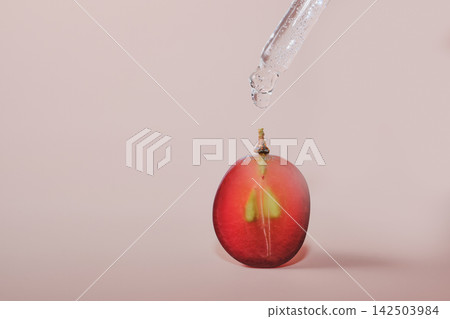 Pipette dropping clear serum onto red grape half, symbolizing natural cosmetic ingredients Pipette dropping clear serum onto red grape half, symbolizing natural cosmetic ingredients 142503984