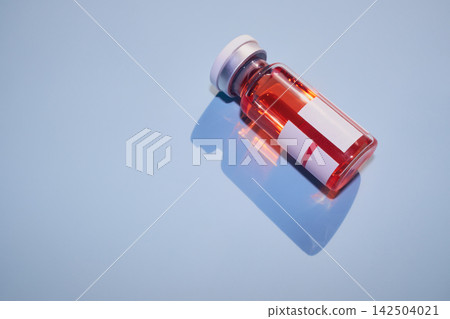 Vial containing red liquid for vaccine or treatment, casting blue shadow Vial containing red liquid for vaccine or treatment, casting blue shadow 142504021