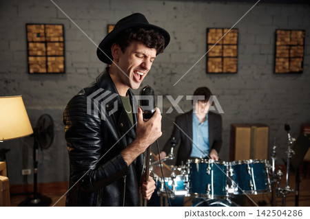 Energetic singer gripping vintage microphone in gritty rehearsal studio Energetic singer gripping vintage microphone in gritty rehearsal studio 142504286