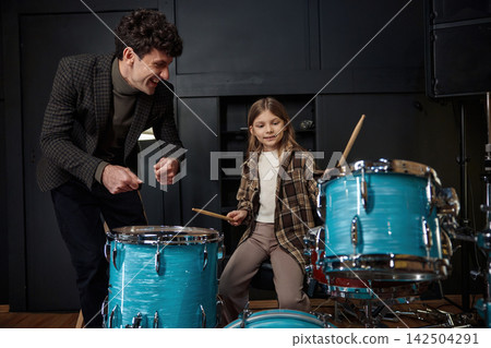 Mentor guides young girl through her drumming lesson in inviting studio setting Mentor guides young girl through her drumming lesson in inviting studio setting 142504291
