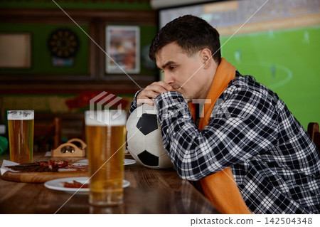 Anxious sports enthusiast firmly grips ball with focused gaze during exciting live broadcast Anxious sports enthusiast firmly grips ball with focused gaze during exciting live broadcast 142504348