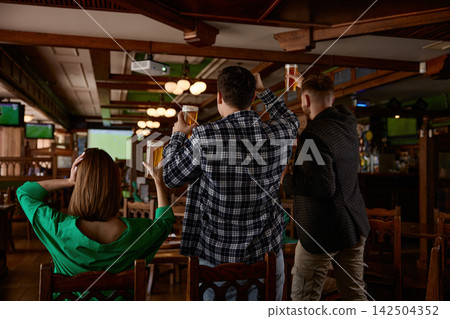 Group of friends celebrating with beer cups enthusiastically with raised arms Group of friends celebrating with beer cups enthusiastically with raised arms 142504352