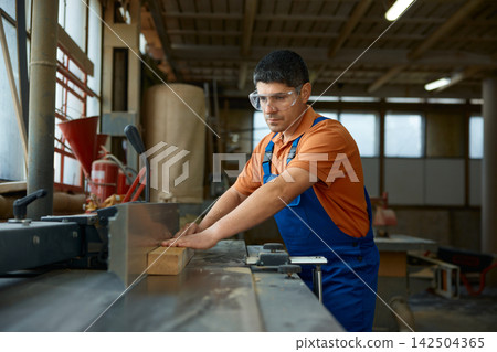 Expert craftsman skillfully smooths wood surface with jointer while ensuring safety and consistency Expert craftsman skillfully smooths wood surface with jointer while ensuring safety and consistency 142504365