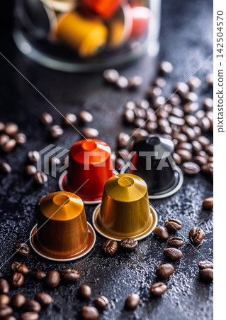 Colorful Coffee Capsules and Espresso Pods Scattered Among Roast Coffee Beans on Dark Surface Colorful Coffee Capsules and Espresso Pods Scattered Among Roast Coffee Beans on Dark Surface 142504570