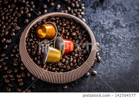 Colorful Coffee Capsules and Espresso Pods Nestled in Bowl of Roasted Coffee Beans on Dark Surface Colorful Coffee Capsules and Espresso Pods Nestled in Bowl of Roasted Coffee Beans on Dark Surface 142504577