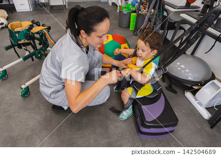 Practicing various skills during physical rehabilitation of a boy patient together with a physical therapist using rehabilitation equipment in a physio center Practicing various skills during physical rehabilitation of a boy patient together with a physical therapist using rehabilitation equipment in a physio center 142504689