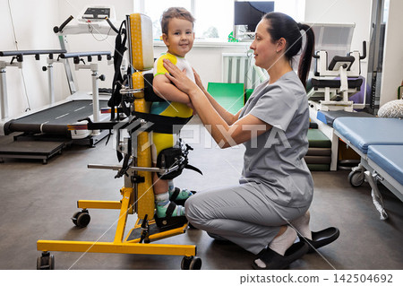 Child works on movement skills with therapist using verticalizer in a rehab setting Child works on movement skills with therapist using verticalizer in a rehab setting 142504692