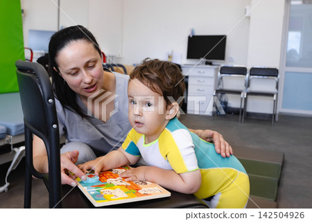 Physical therapist motivates a boy to do difficult rehabilitation exercises with a reward in the form of interesting toys. Children's rehabilitation Physical therapist motivates a boy to do difficult rehabilitation exercises with a reward in the form of interesting toys. Children's rehabilitation 142504926
