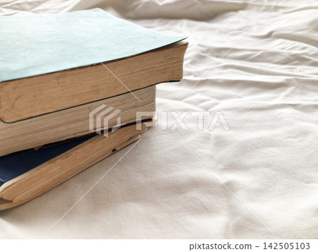 Weekend reading and relaxation time in the bedroom; old books piled on white sheets; reading habit; lifestyle Weekend reading and relaxation time in the bedroom; old books piled on white sheets; reading habit; lifestyle 142505103