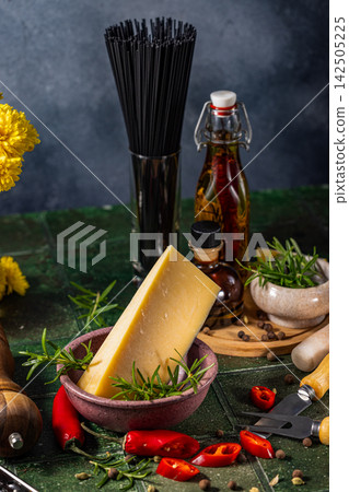 Piece of hard cheese with rosemary, chili pepper and black spaghetti on table 142505225