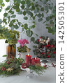 A natural floral arrangement featuring red candles, a Christmas wreath, and the green of eucalyptus. 142505301