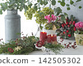 A natural floral arrangement featuring red candles, a Christmas wreath, and the green of eucalyptus. 142505302