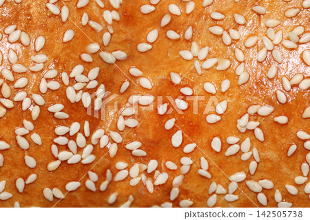Golden brown baked bread covered with numerous white sesame seeds creates an appetizing closeup food texture with a warm crispy crust. Golden brown baked bread covered with numerous white sesame seeds creates an appetizing closeup food texture with a warm crispy crust. 142505738