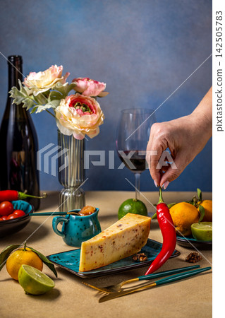 Woman adding chili pepper to cheese board with wine and fruits Woman adding chili pepper to cheese board with wine and fruits 142505783