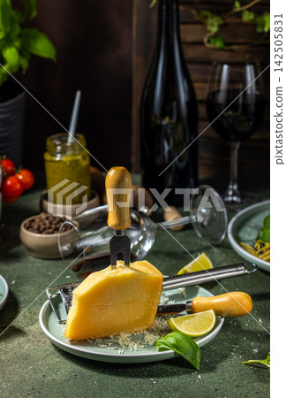 Wedge of parmesan cheese with grated cheese on plate, wine and pesto for italian dinner Wedge of parmesan cheese with grated cheese on plate, wine and pesto for italian dinner 142505831
