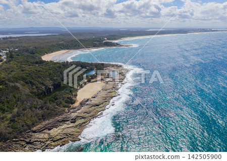 Aerial view of the Blue Pool, Green Pool and natural rock pool surrounded by rugged coastal landscape and vegetation, with Spooky Beach and the Pacific Ocean in the background at Angourie on the NSW Aerial view of the Blue Pool, Green Pool and natural rock pool surrounded by rugged coastal landscape and vegetation, with Spooky Beach and the Pacific Ocean in the background at Angourie on the NSW 142505900