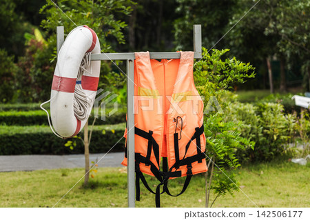 Orange Life Jackets and Lifebuoy Hanging Beside Landscaped Garden Orange Life Jackets and Lifebuoy Hanging Beside Landscaped Garden 142506177