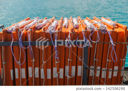 Stacked Orange Life Jackets Secured on Ferry Above Turquoise Sea Stacked Orange Life Jackets Secured on Ferry Above Turquoise Sea 142506298