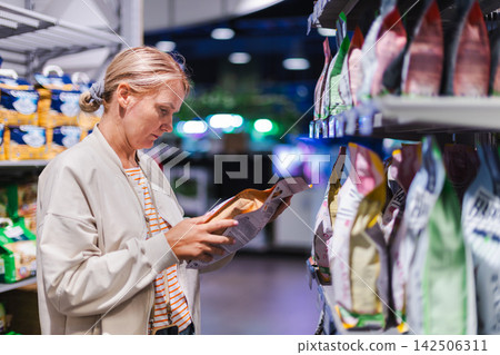 Woman Reading Packaged Pet Food Label in Store Woman Reading Packaged Pet Food Label in Store 142506311