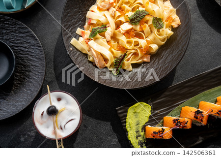 Seafood menu. Tasty recipe. Spaghetti with salmon pieces ikura roe chard leaves in creamy sauce served with wasabi sushi roll cocktail drink. Seafood menu. Tasty recipe. Spaghetti with salmon pieces ikura roe chard leaves in creamy sauce served with wasabi sushi roll cocktail drink. 142506361