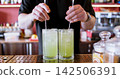 Preparing beverage. Pub service. Male barkeeper hand mixing cold green pistachio syrup cocktail with sparkling water spoon in glass. 142506391