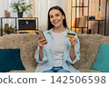 Young woman on sofa carefully entering credit card details on smartphone making online payment 142506598